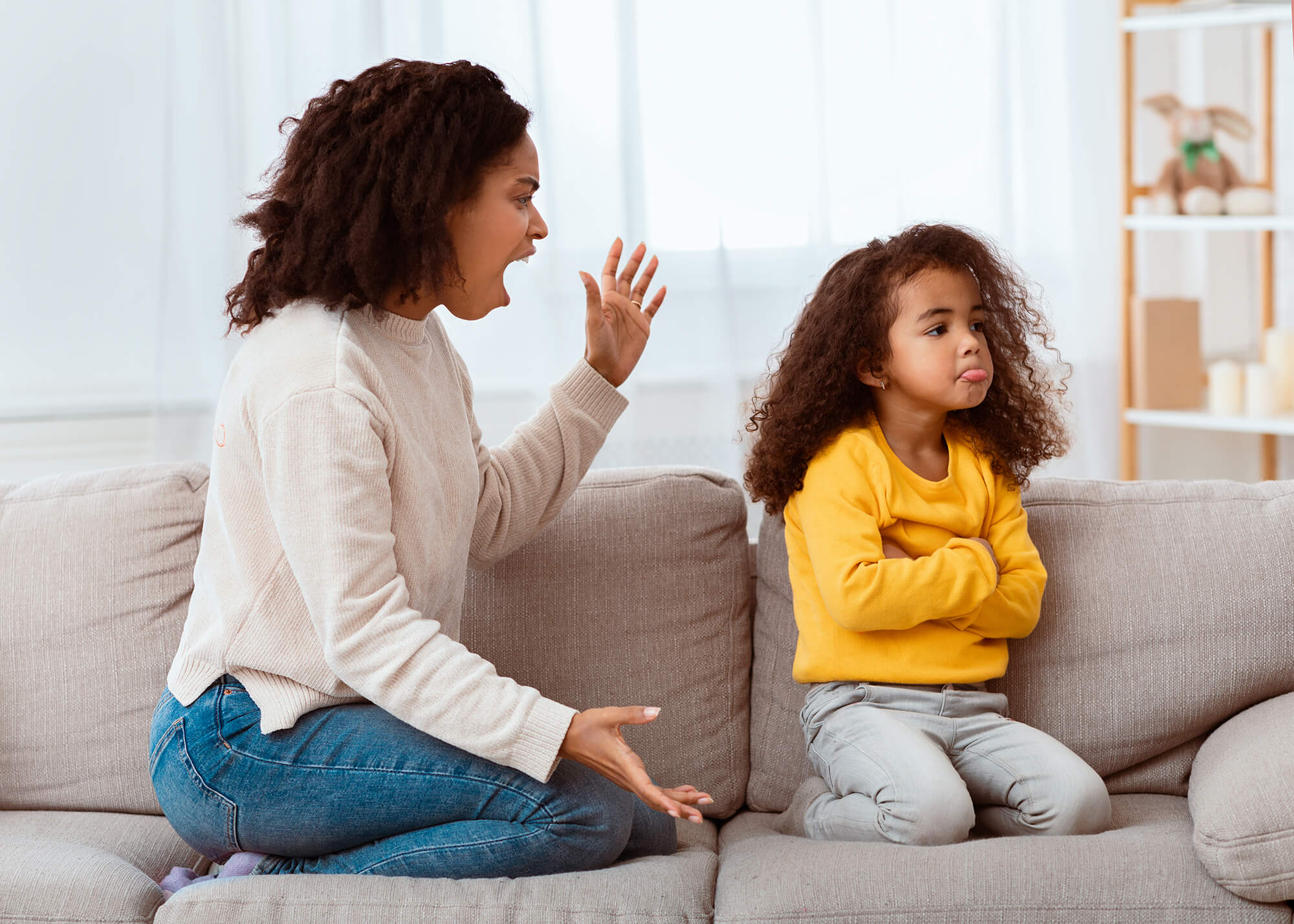A parent and young child sitting on a couch mid-disagreement
