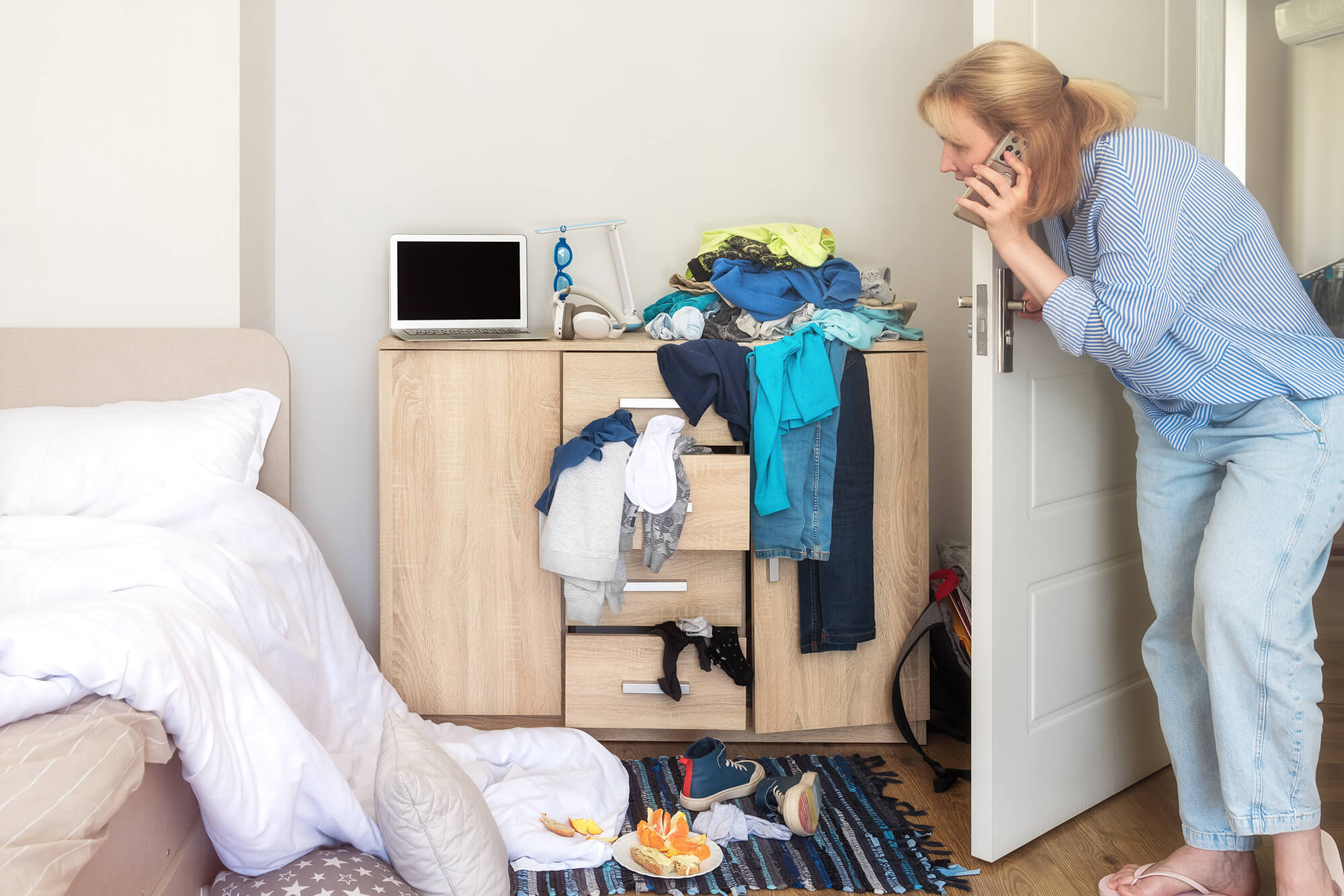 A parent looking into a child’s messy bedroom while on the phone